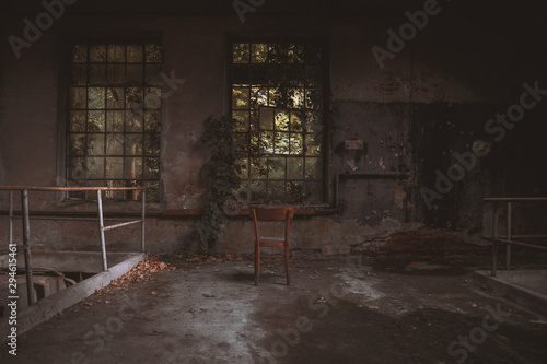 Wooden chair in front of an old and broken window within an abandoned building
