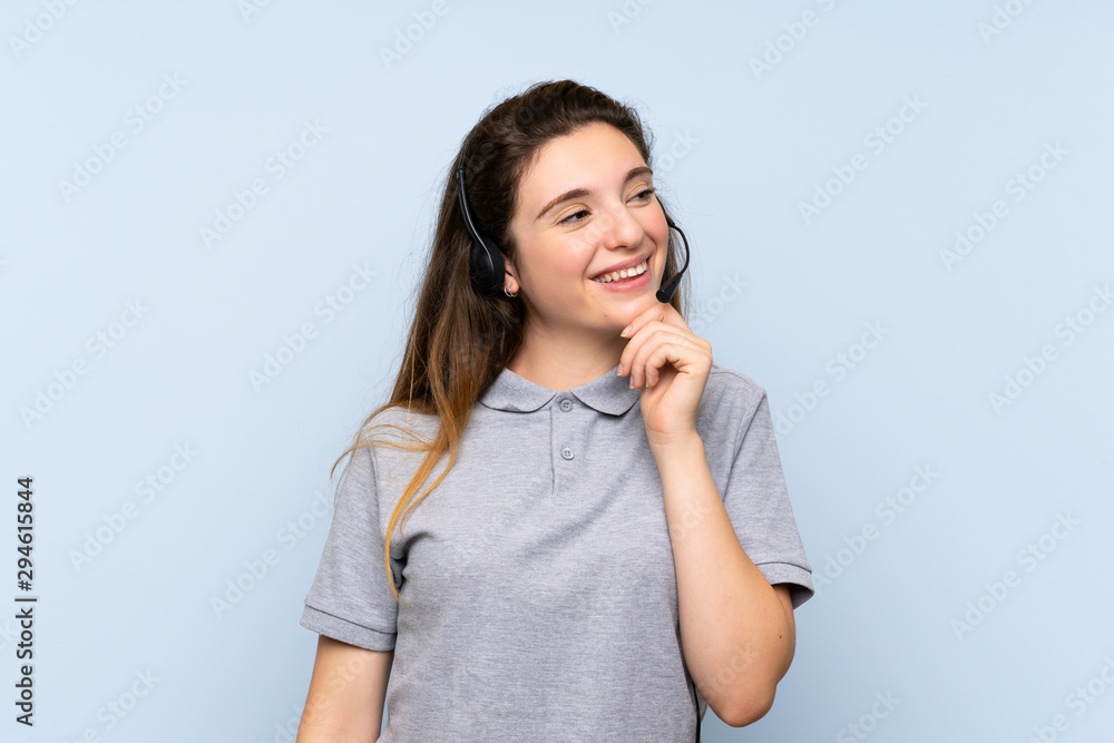 Young brunette girl over isolated blue background working with headset looking side Young brunette girl over isolated blue background working with headset looking side