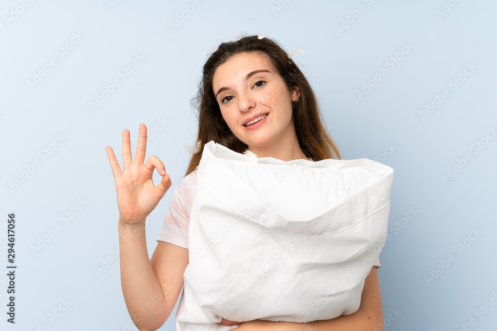 Young woman in pajamas over isolated blue background showing ok sign with fingers - obrazy, fototapety, plakaty 