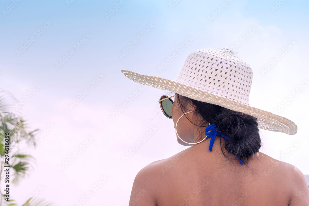 Woman back wearing sunglass and hat over sky background