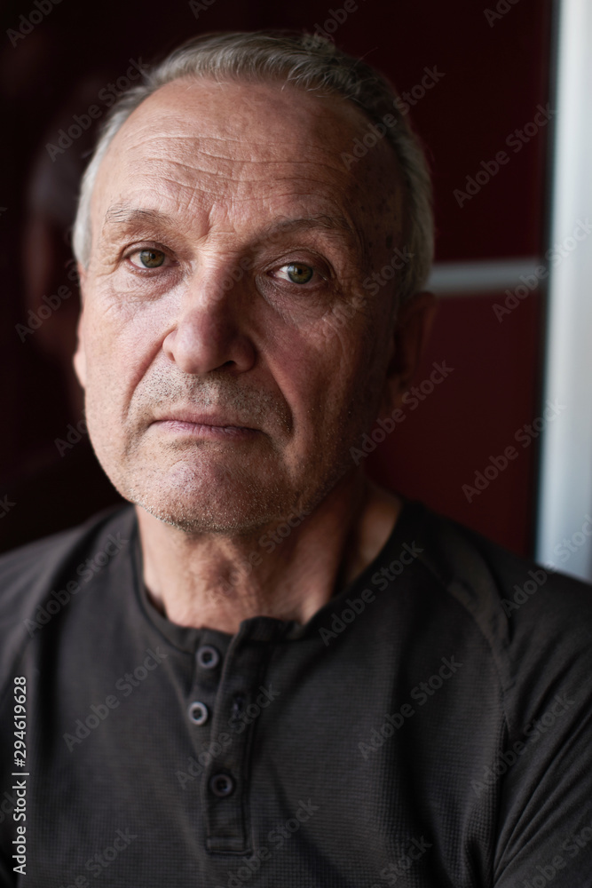 Obraz premium Portrait of serious handsome elderly man with gray hair, stylishly dressed , looking at camera against the background of window