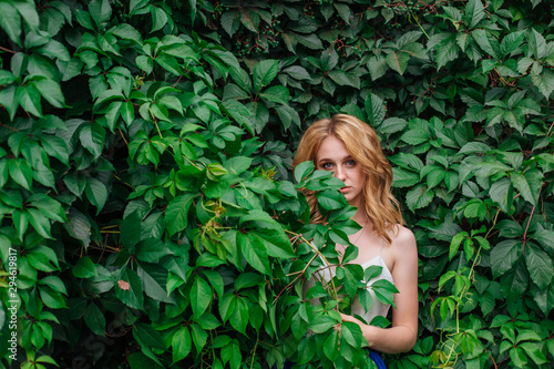 Portrait of a young beautiful woman  standing next to the wall of wild grape leaves.