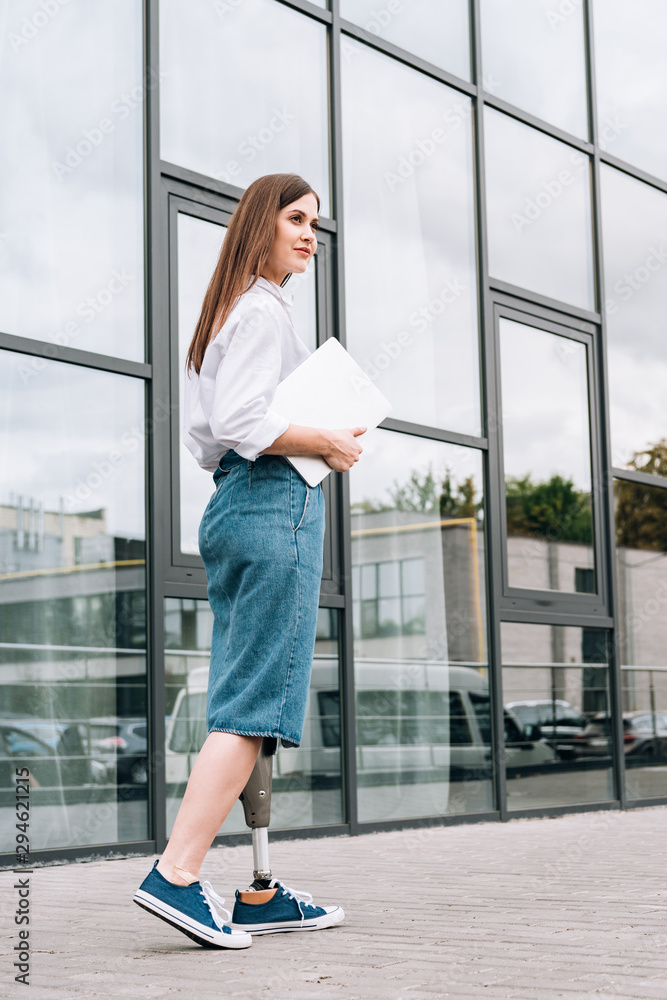 full length view of disabled woman in denim skirt holding laptop on street full length view of disabled woman in denim skirt holding laptop on street