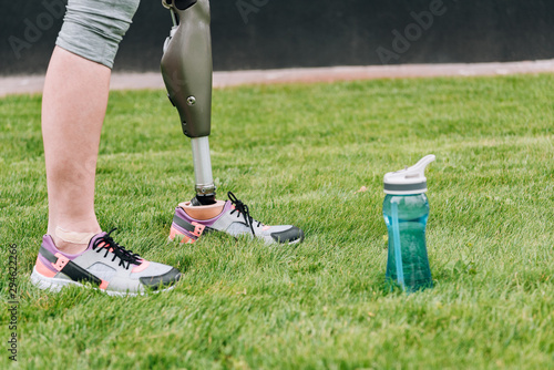 partial view of disabled sportswoman standing near sport bottle on grass