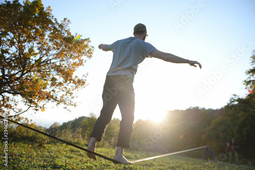young active male guy barefoot in cap walking balancing on long tensioned rope during outdoor sport leisure activity in natural harmony environment