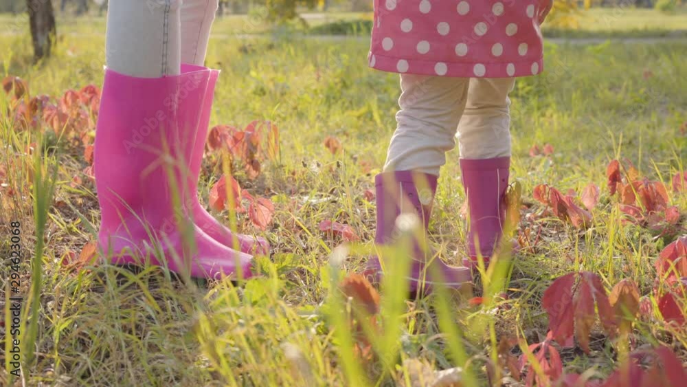 Close-up of two females in pink rubber boots standing on the autumn ...