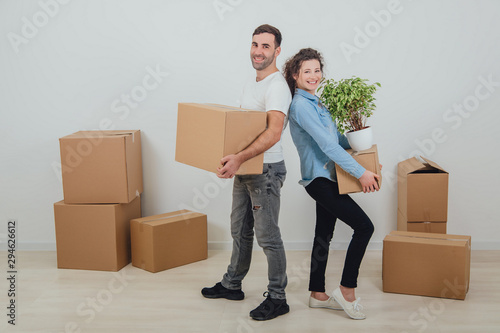 Happy wife and husband holding carton boxes, standing back to back, smiling extremely satisfied to move into new apartment.