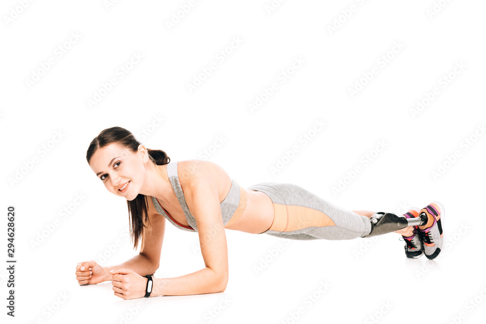 Fototapeta premium smiling disabled sportswoman with prosthesis standing in plank isolated on white