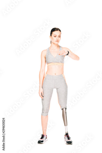 full length view of sportswoman with prosthetic leg looking at smartwatch isolated on white