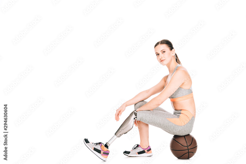 Fototapeta premium disabled sportswoman sitting on basketball ball isolated on white