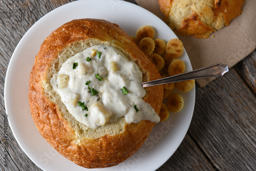 Overhead shot of a bread bowl of New England Style Clam Chowder with oyster crackers on a rustic wood table. photo