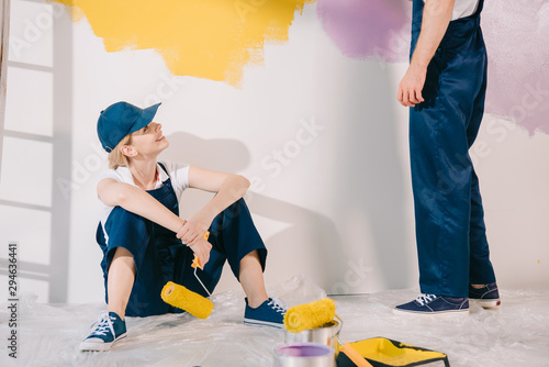 attractive young painter in uniform sitting on floor and looking at man in uniform