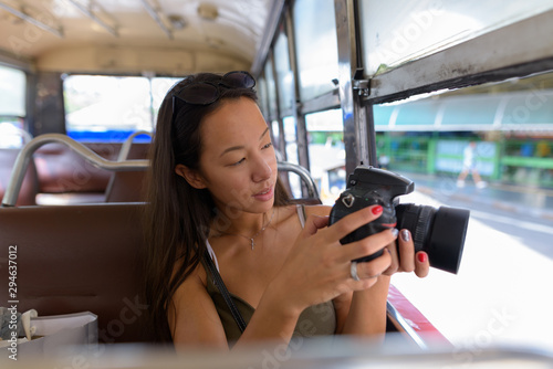 Young tourist woman sitting at bus while using DSLR camera
