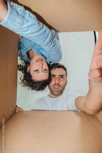 Curious wife and husband unpacking, reaching things from carboard box, looking surprised.