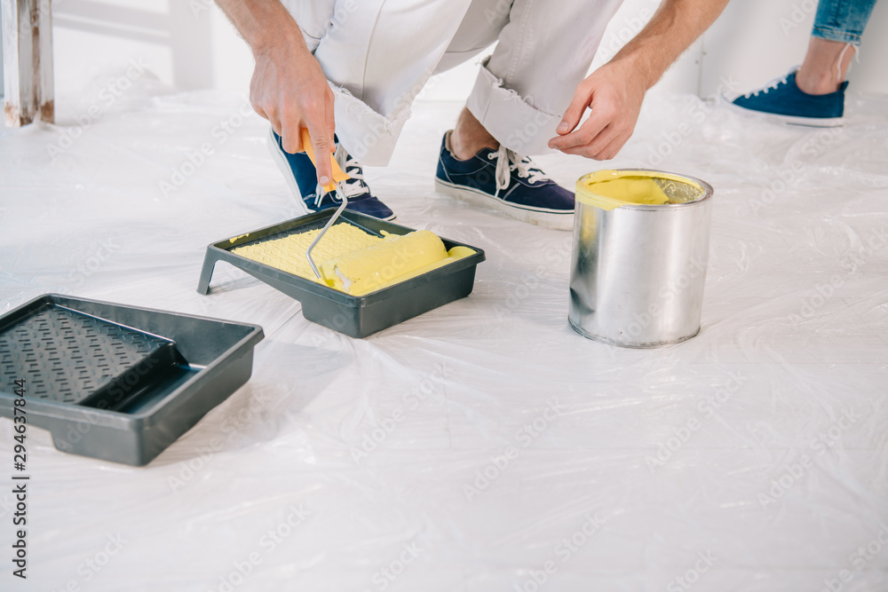 cropped view of man putting paint roller into yellow paint cropped view of man putting paint roller into yellow paint