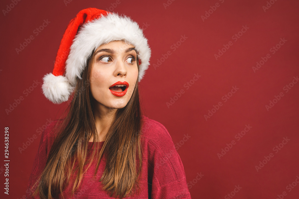 Christmas Santa hat woman portrait. Smiling amazed happy girl isolated against red background. Free copyspace for text. New year concept. Christmas Santa hat woman portrait. Smiling amazed happy girl isolated against red background. Free copyspace for text. New year concept.