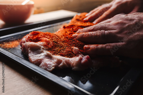 Fototapeta Naklejka Na Ścianę i Meble -  Man preparing raw piece of meat, rubbing different spices and herbs in it before roasting