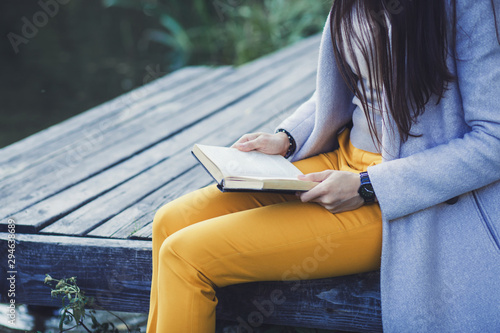 a woman sits wood bridge and holds a book in autumn park