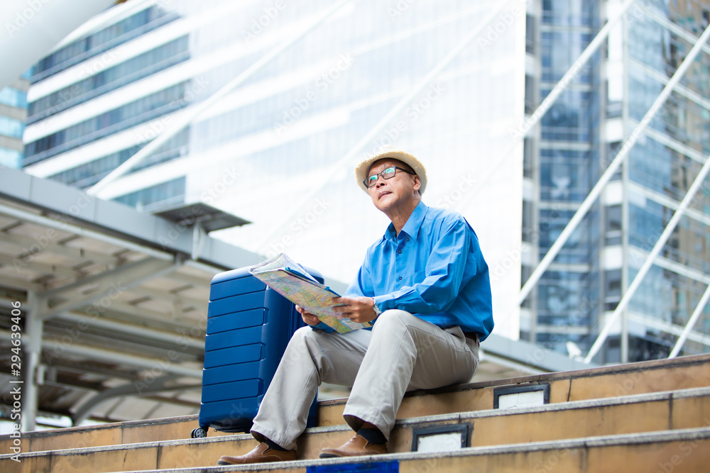 Senior man traveling with luggage sitting on staircase checking city map and sightseeing Travel and tourism concept.Elderly Travel and tourism concept.