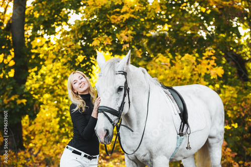 Pretty blonde woman with white horse in autumnal nature.