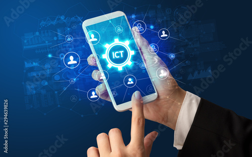 Fotografie Female hand holding smartphone with ICT abbreviation, modern technology concept