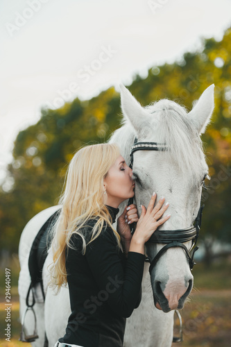 Young attractive blond woman kiss a white horse.