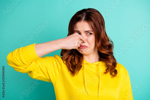 Photo of disgusted girl smelling something bad nasty looking shutting her nose isolated over vivid turquoise color background photo