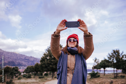 young backpacker woman hiking in nature. Cloudy winter day. Using mobile phone to take a picture