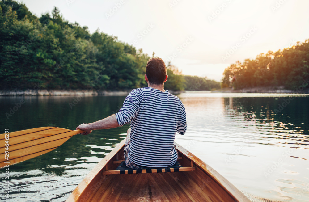 Man in sailor shirt paddling canoe on the sunset lake	