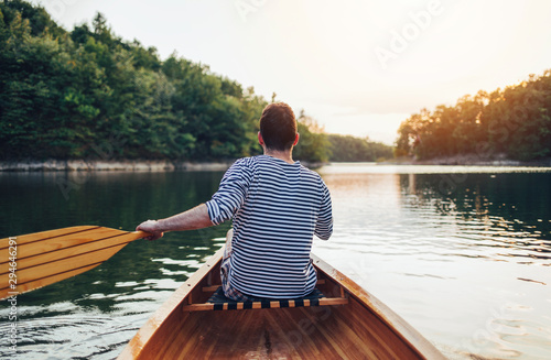 Man in sailor shirt paddling canoe on the sunset lake 