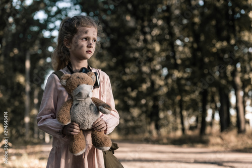 cute kid holding dirty teddy bear near trees in chernobyl, post apocalyptic concept