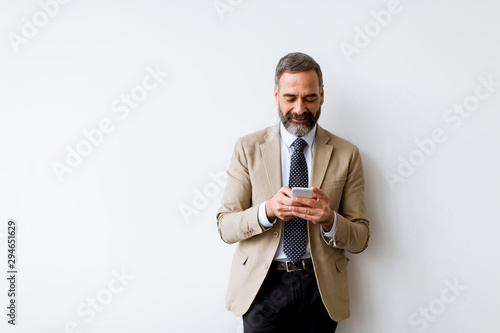 Senior businessman using mobile phone against wall in office