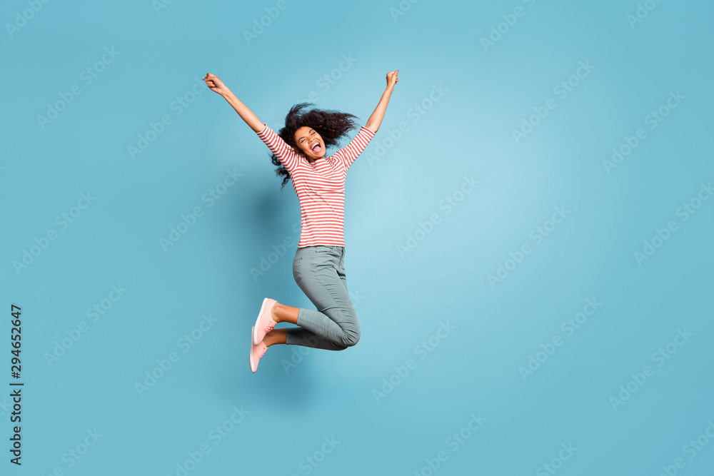 Full length body size profile side photo of screaming shouting cheerful cute nice girlfriend screaming with happiness jumping up isolated over blue pastel color background in striped t-shirt Full length body size profile side photo of screaming shouting cheerful cute nice girlfriend screaming with happiness jumping up isolated over blue pastel color background in striped t-shirt