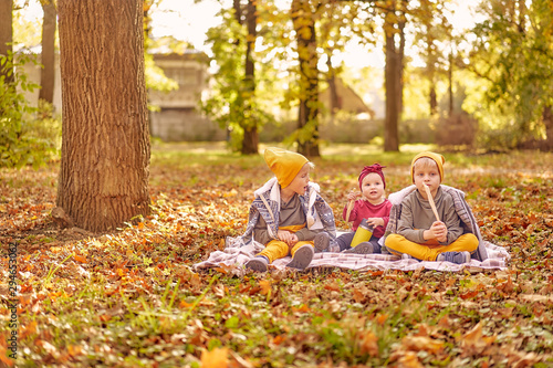 Three children on the lawn in the park on a sunny autumn day. two brothers and an infant girl sister eat crackers in the park and drink tea from a thermos.