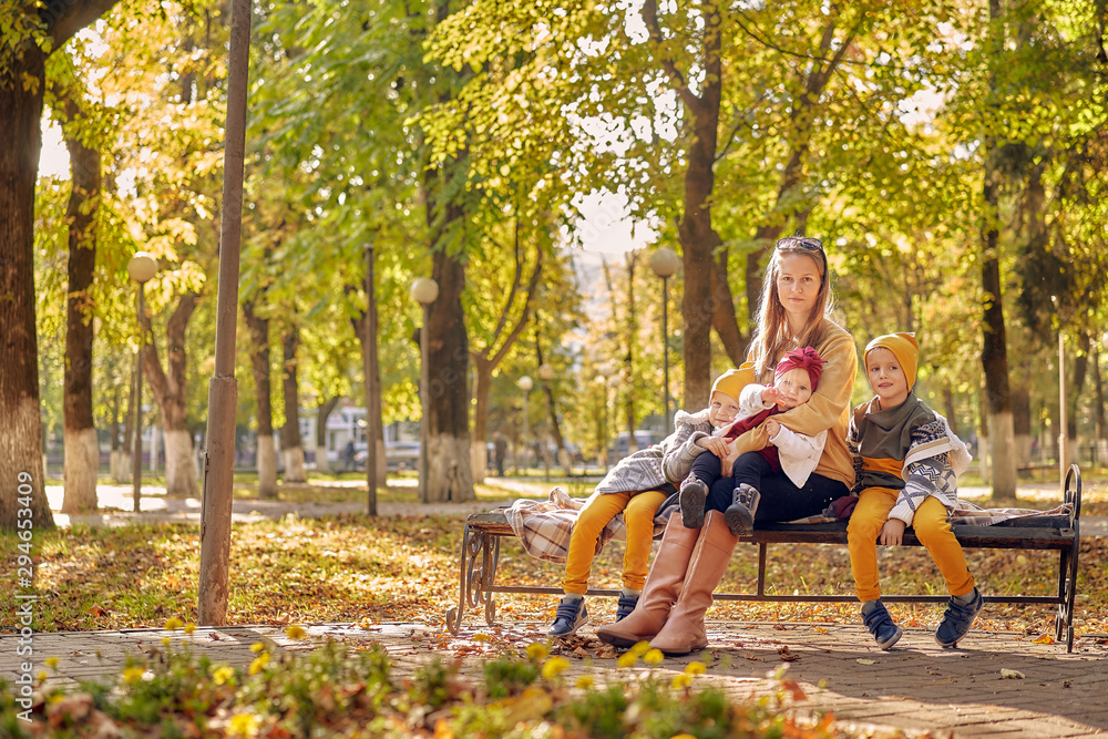 family have a rest on a warm autumn day in the park. Mom and three children on a bench. mom holds daughter on her lap.