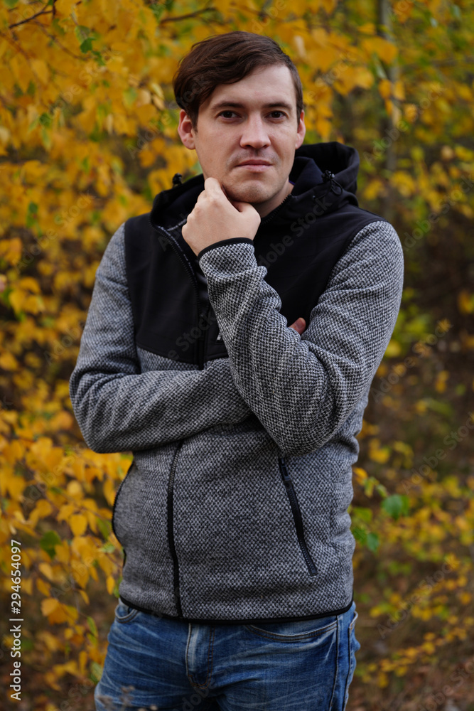 Portrait of a young handsome man in casual clothes against the yellowed trees in the autumn forest.
