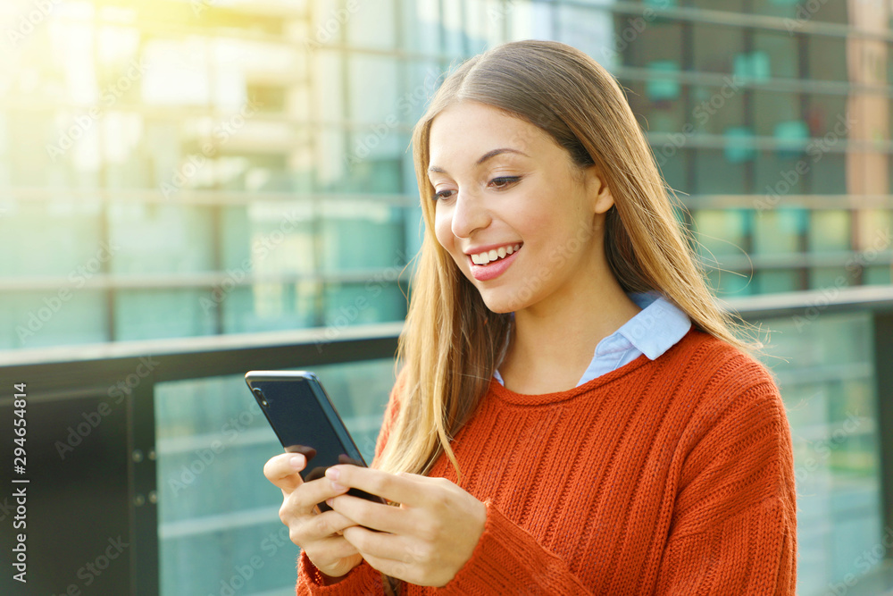 Young business woman wearing orange sweater texting on the smart phone out of the office in a sunny day.