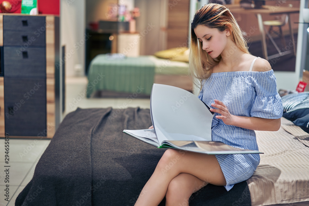 young girl watching a catalog in a furniture store sitting on a sofa young girl watching a catalog in a furniture store sitting on a sofa