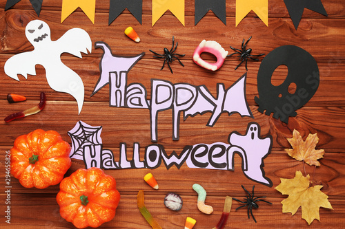 Text Happy Halloween with ghosts, dry leafs and pumpkins on wooden background