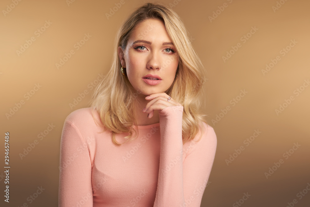 Studio portrait of blonde girl with green eyes and fair skin, pink sweater against a brown backdrop Studio portrait of blonde girl with green eyes and fair skin, pink sweater against a brown backdrop