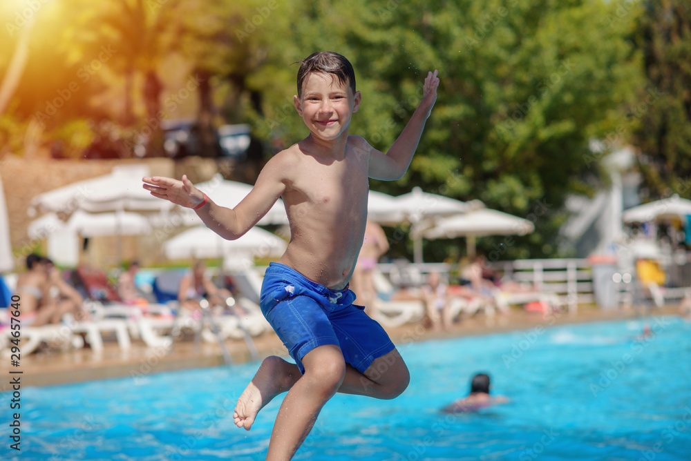 Portrait of cheerful  jumping European boy swimming in pool. He is enjoying his summer vacations.