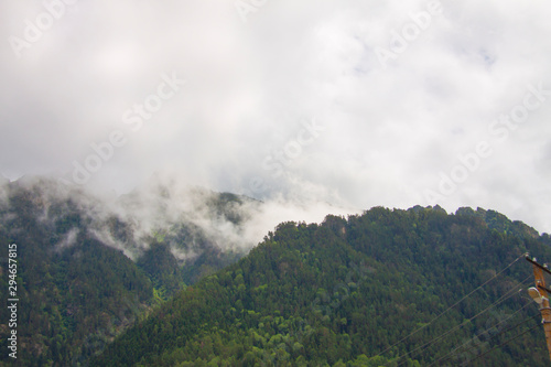Beautiful panorama of the Caucasus mountains. Top of mountain range is covered in fog. Clouds lie on mountains. Summer day. Background image for travel and nature.