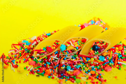 Abstract food background. Durum wheat pasta and colorful candies over yellow background. Incompatible products concept.