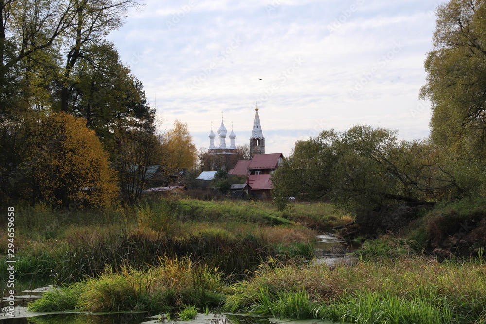 Country landscape with village church and houses on riverside in sunny autumn day Country landscape with village church and houses on riverside in sunny autumn day