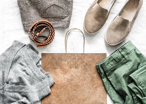 Set of women's fashion clothes - pullover, cotton pants, suede sports shoes, leather belt and paper bag on a light background. Shopping, sale concept