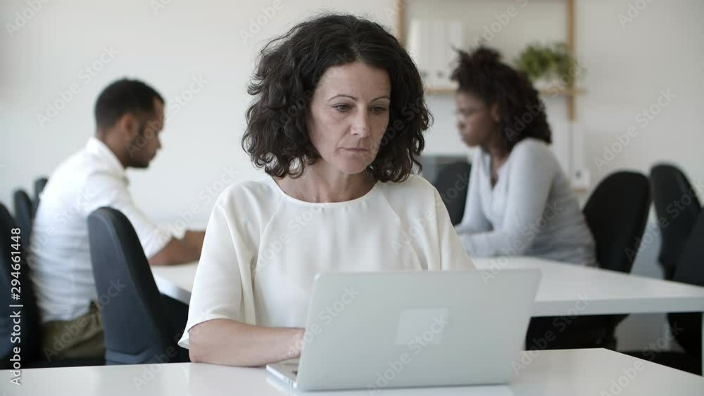 Focused mature woman working with laptop in office. Thoughtful middle aged lady using modern device. Technology concept Focused mature woman working with laptop in office. Thoughtful middle aged lady using modern device. Technology concept