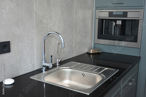 Modern kitchen with chrome faucet, water tap, black kitchen table, coffee mashine and kitchen sink.