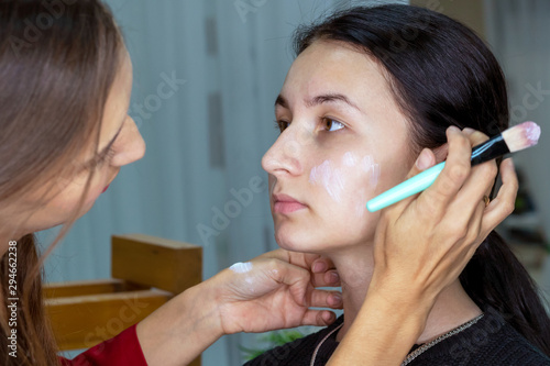 Close-up portrait of woman applying cosmetic Foundation on face using makeup brush. Makeup artist stylist doing makeup