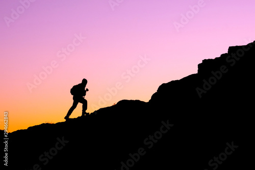 the silhouette of a man climbing a mountain in the sunset light