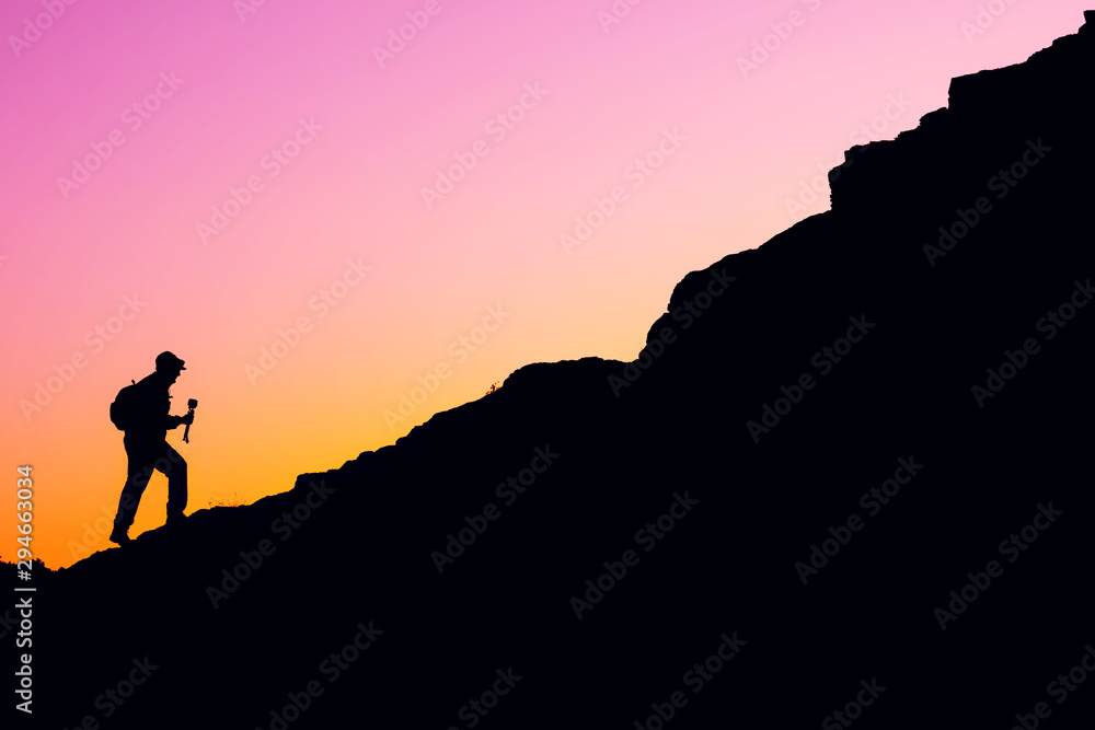 silhouette of a man with a backpack against the red sky at the beginning of a steep climb